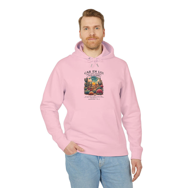 Un homme porte un sweat à capuche rose avec une illustration de désert et un verset biblique.
