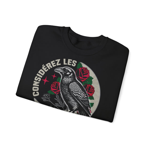 Sweat-shirt noir plié avec une illustration de corbeau, de roses et l'inscription Considérez les.