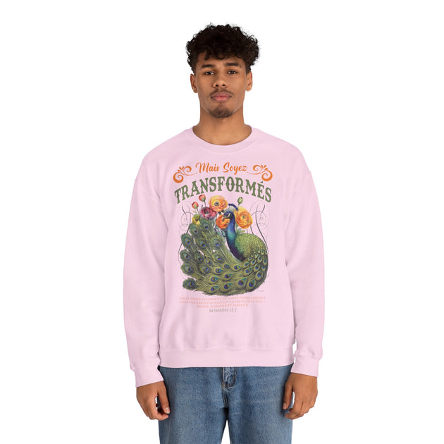 Un homme porte un sweatshirt rose clair orné d'un paon et du texte Mais soyez transformés.