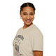 Une femme porte un t-shirt beige en coton avec une empreinte de main et un texte religieux.