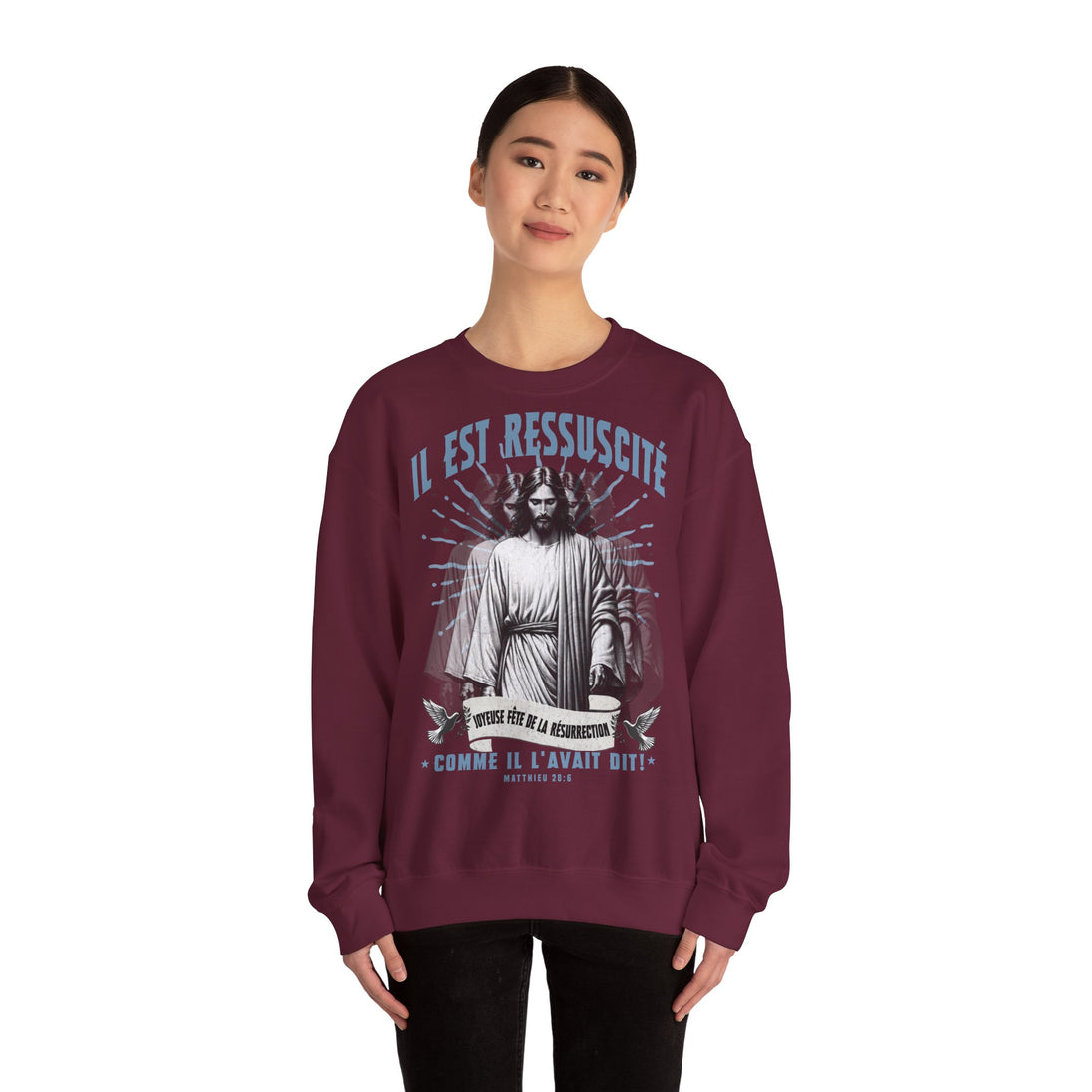 Une femme porte un sweatshirt bordeaux avec une illustration religieuse et le texte Il est ressuscité.