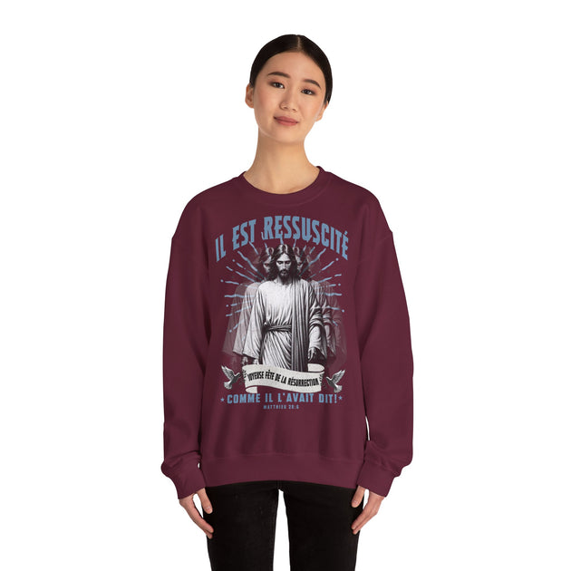 Une femme porte un sweatshirt bordeaux avec une illustration religieuse et le texte Il est ressuscité.