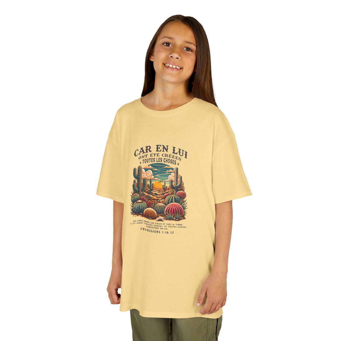 Un enfant porte un t-shirt jaune pâle avec une illustration de cactus et un texte religieux.