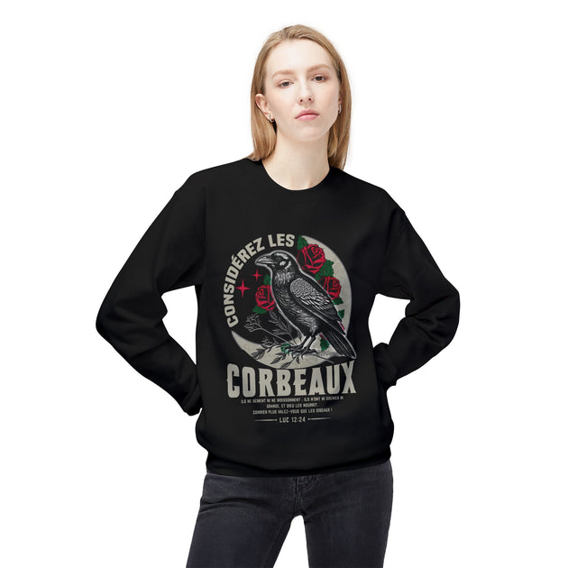 Une femme porte un sweatshirt noir avec une illustration de corbeau, de roses et le texte Luc 12:24.