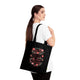 Une femme porte un tote bag noir en coton orné d'un motif floral et du texte Dieu est bon.