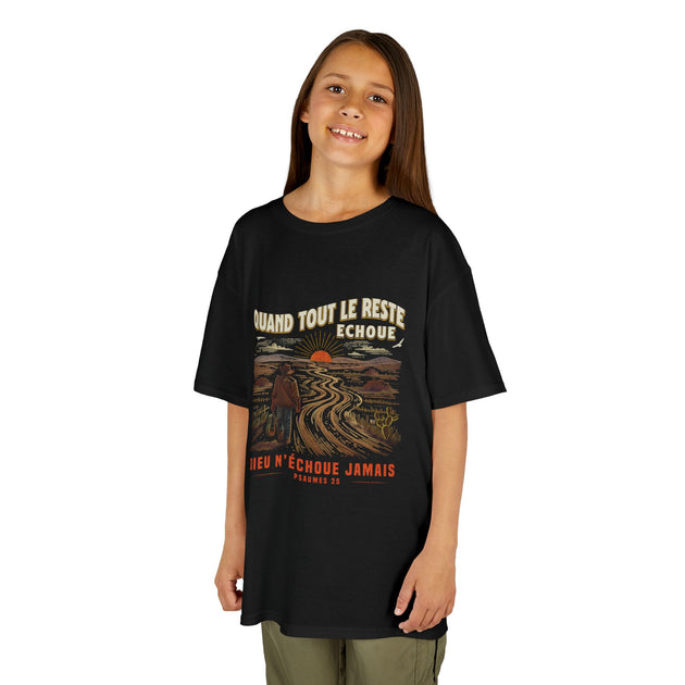 Une enfant porte un t-shirt noir avec une illustration rétro de paysage et un texte religieux.