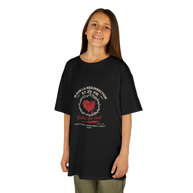 Une jeune fille porte un t-shirt noir en coton avec un motif religieux et du texte en français.
