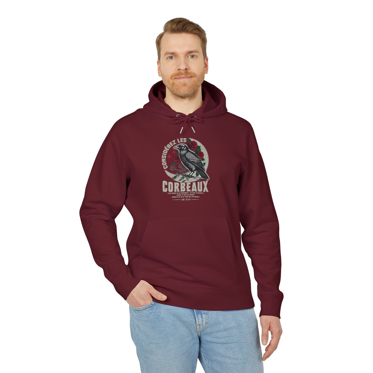 Un homme porte un sweat à capuche bordeaux avec une illustration de corbeau et un texte religieux.