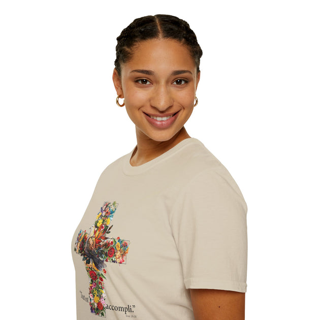 Une femme porte un t-shirt beige orné d'une croix fleurie et de l'inscription Tout est accompli.