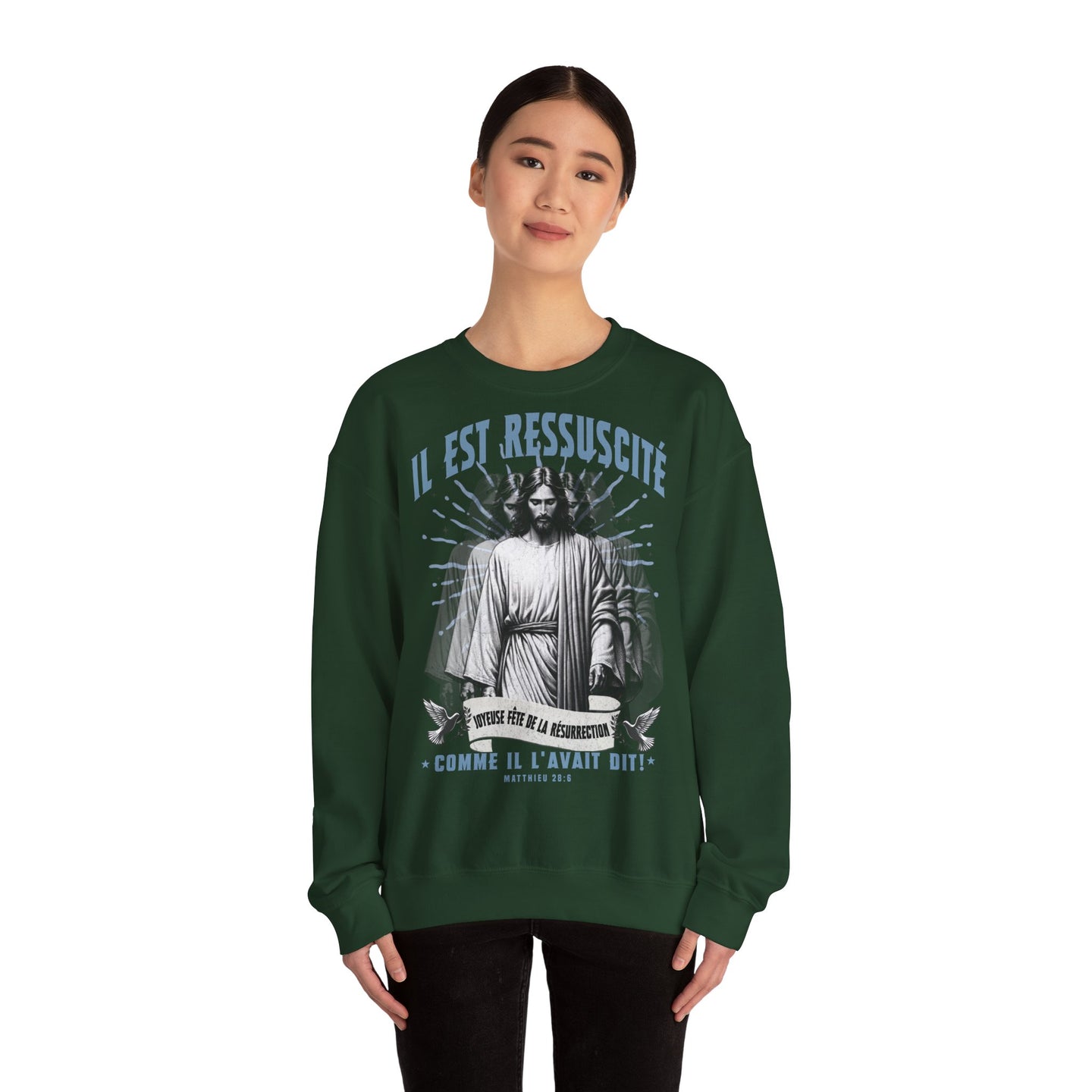 Une femme porte un sweatshirt vert foncé avec une illustration religieuse et le texte Il est ressuscité.