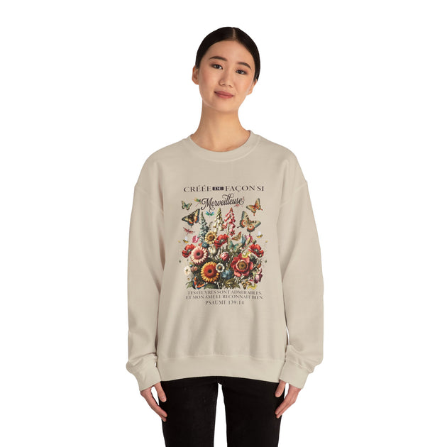 Une femme porte un sweat-shirt beige orné d'un motif floral et d'un texte religieux en français.