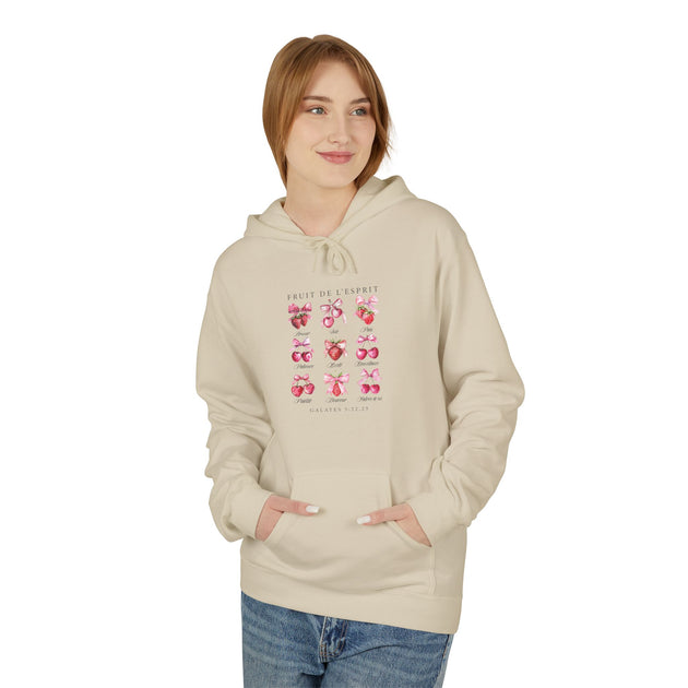 Une femme porte un sweat à capuche beige orné d'un motif de fruits et de nœuds roses.